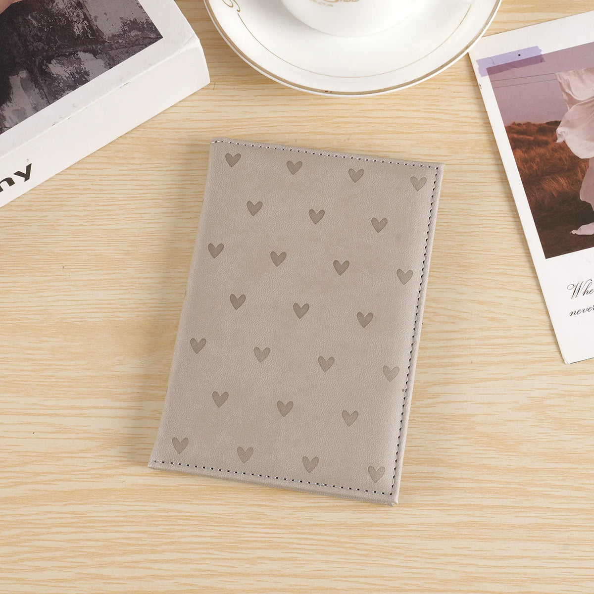 A light gray leather passport cover with a subtle pattern of small heart prints resting on a wooden surface.