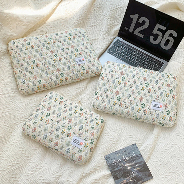 A floral pattern laptop sleeve resting on a cream-colored textured fabric next to an open laptop.