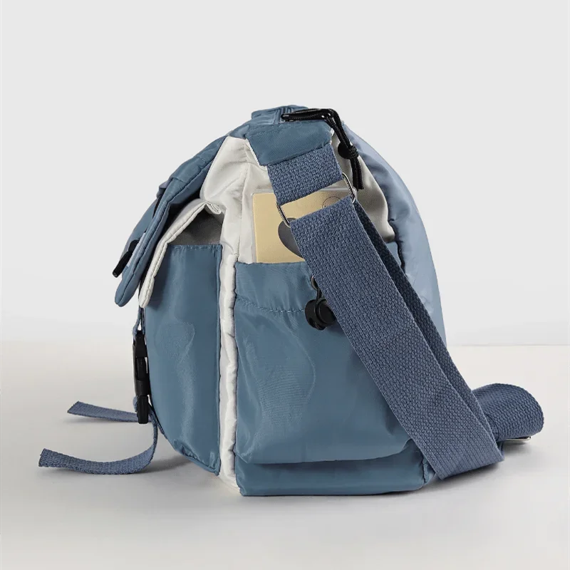 Bolso cruz de nylon azul claro con correa beige y ribete blanco contra fondo blanco.