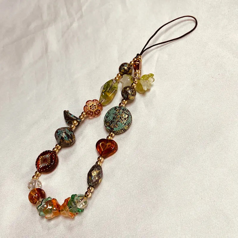 A delicate beaded phone charm strap with various colored stones and a thin cord.