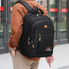 A person wearing a brown shirt is carrying a black TY Fashionbag backpack outdoors.