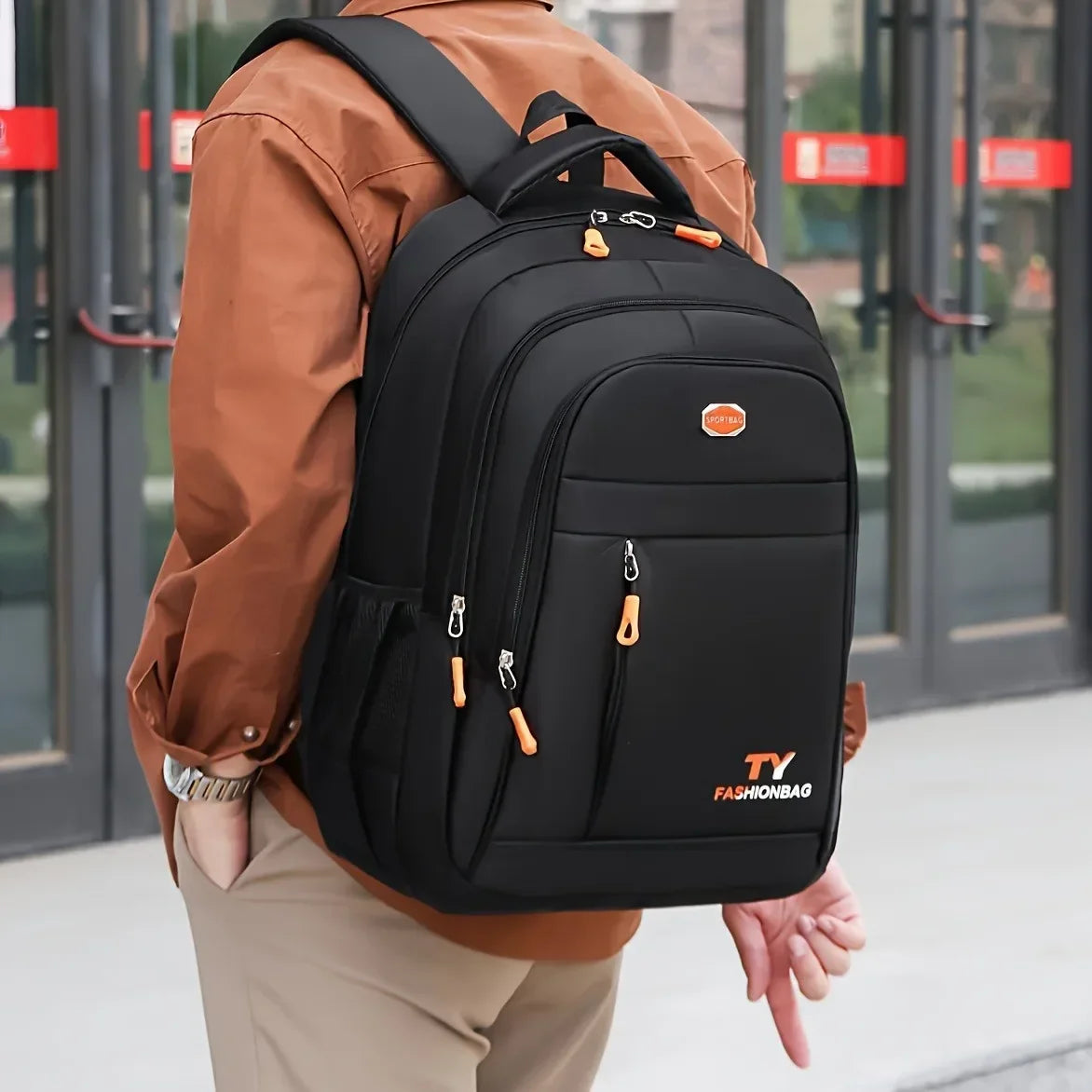 A person wearing a brown shirt is carrying a black TY Fashionbag backpack outdoors.