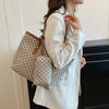 A woman holds a beige geometric patterned tote bag with brown leather trim against a white background.