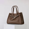 A brown genuine leather women's shoulder tote bag with a flap closure displayed on a white pedestal.