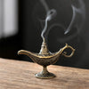 Antique metal incense burner with a spout and handle emitting smoke on a wooden surface.