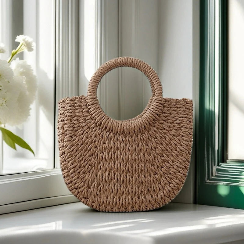 A natural beige handwoven rattan beach bag resting on a white windowsill next to a window frame.
