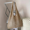A beige bohemian knit shoulder bag hanging on a silver display rack.