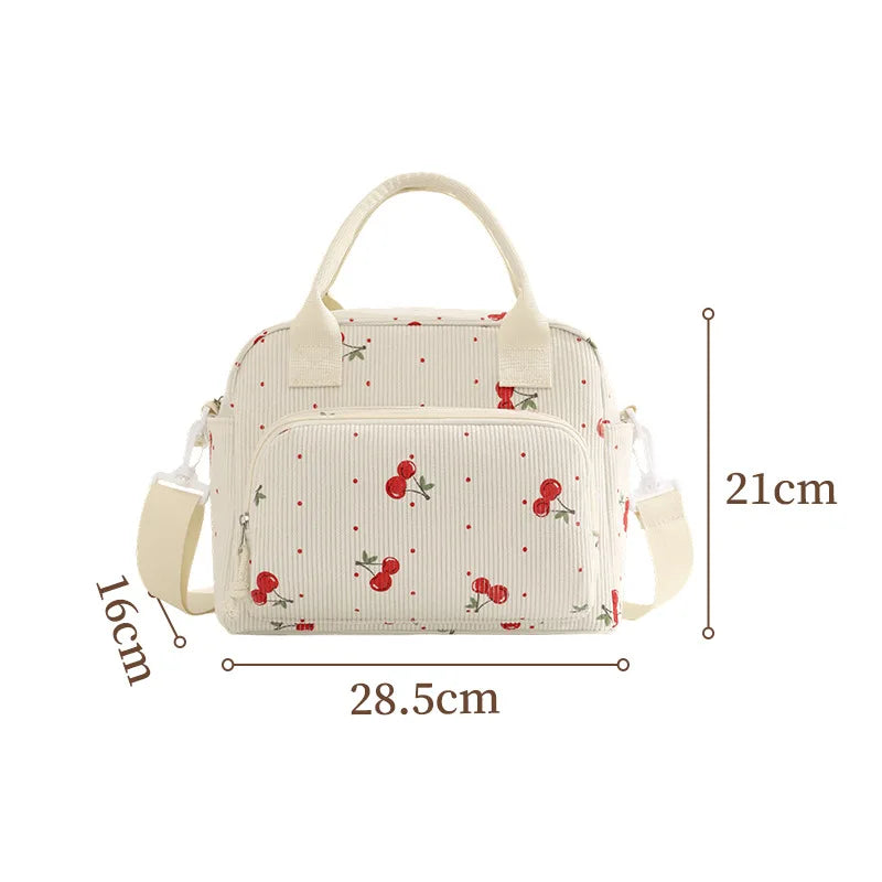 A cream-colored floral corduroy insulated lunch bag with light green and red fruit patterns.