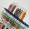 A collection of multicolor acrylic chain bracelets in various shades of brown, blue, white, and green.