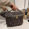 A close-up of a dark gray faux suede cosmetic bag with a leopard print pattern being held by a hand.