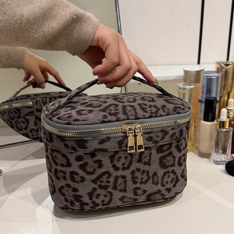 A close-up of a dark gray faux suede cosmetic bag with a leopard print pattern being held by a hand.