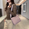 A woman wearing a brown knit sweater and beige pants carries a light pink nylon crossbody bag in a modern indoor setting.