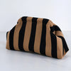 A beige and black striped summer crochet handbag is shown lying on a white surface.