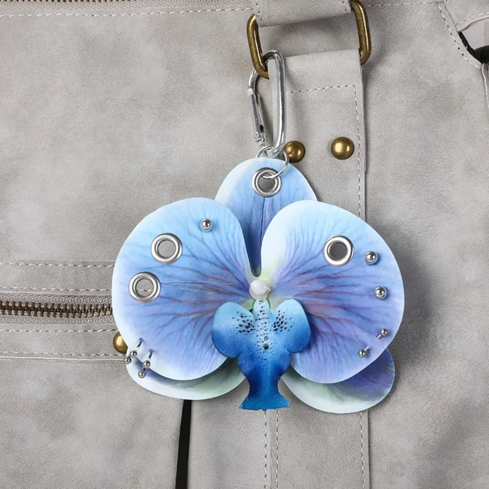 A realistic blue and purple phalaenopsis orchid flower keychain attached to a gray leather bag.