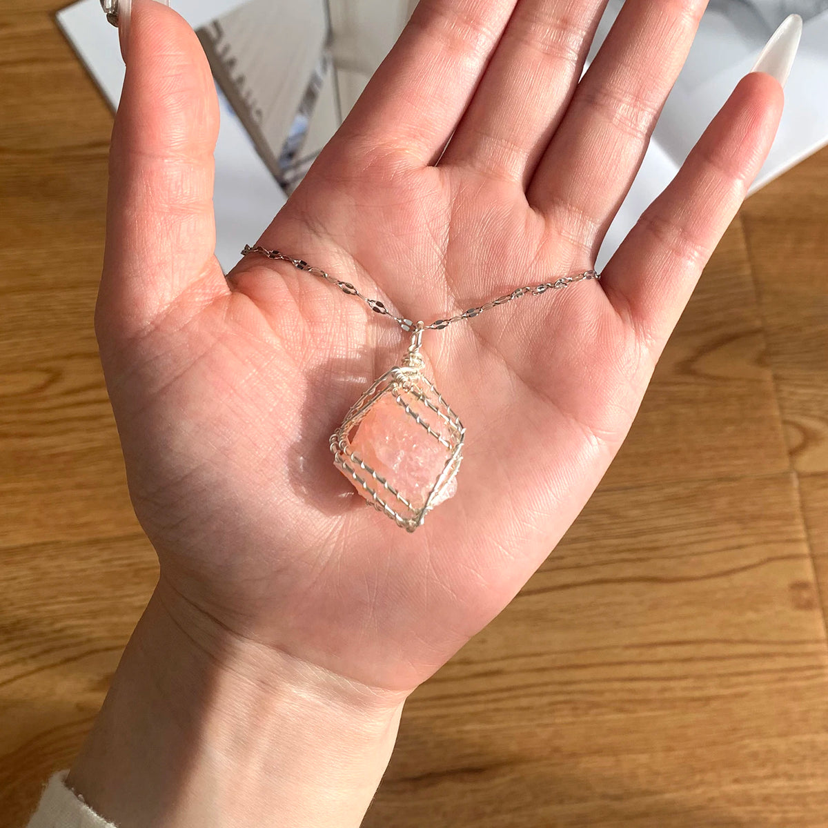 A hand holds a handcrafted amethyst crystal pendant necklace featuring a copper wire wrap.