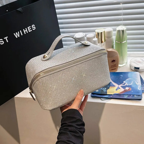 A hand holds a silver textured cosmetic organizer bag next to various beauty products.