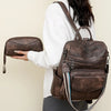 A woman holds a brown retro PU leather travel backpack with a tassel detail.