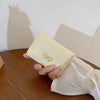 Une main tient un porte-cartes portefeuille tri-pli en PU beige clair sur une surface en bois.