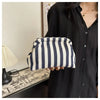 A hand holds a striped crochet tote bag with a shell accent against a dark shirt.