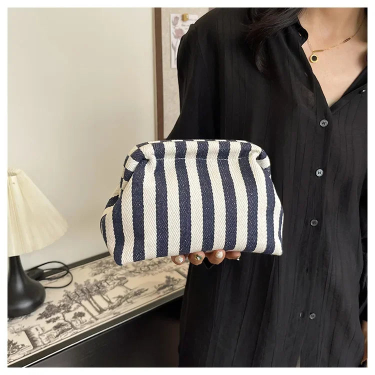 A hand holds a striped crochet tote bag with a shell accent against a dark shirt.