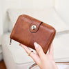 A brown leather wallet with a silver clasp is held in a person's hand against a light background.