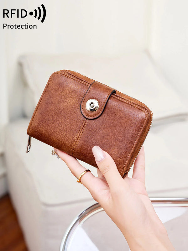 A brown leather wallet with a silver clasp is held in a person's hand against a light background.