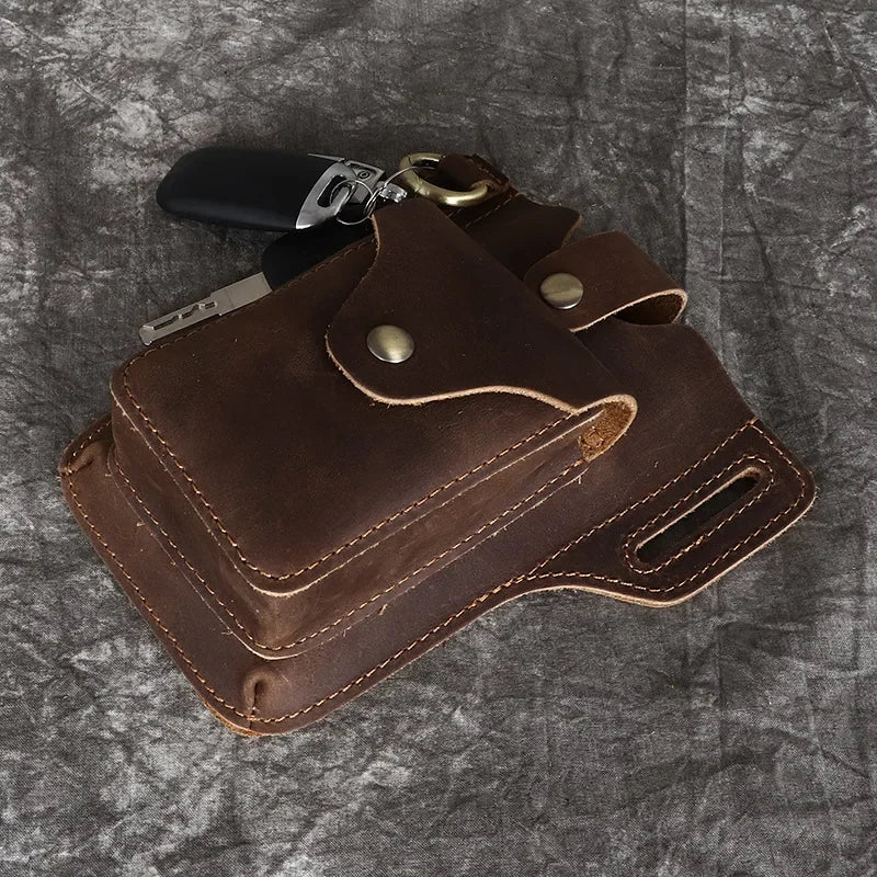 A brown genuine leather men's waist bag with a black leather strap and metal hardware resting on a gray textured surface.
