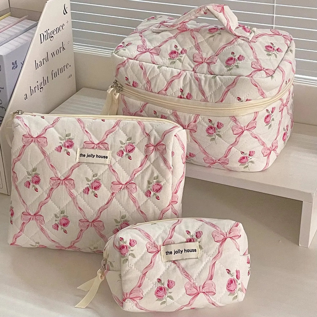 A pink and white quilted floral embroidered makeup bag is displayed next to a larger version.