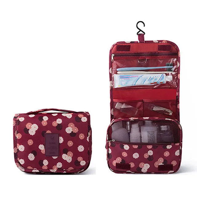 A maroon multi-compartment travel pouch with a floral print, featuring zippered sections and a hanging loop.