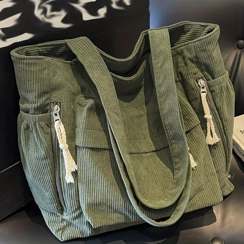 Sac cabas vert en velours côtelé avec plusieurs poches et sangles, exposé sur une surface sombre.
