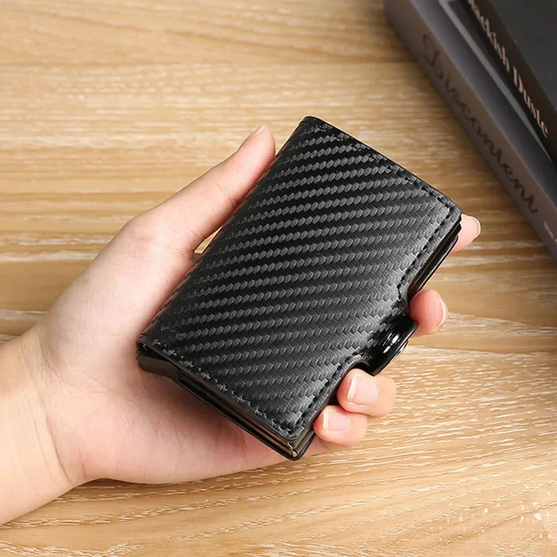 A hand holds a black textured double layer ID card holder wallet on a wooden surface.