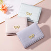 Un ensemble de trois porte-cartes pliants en PU rose pâle et lavande avec des ornements de nœud doré.