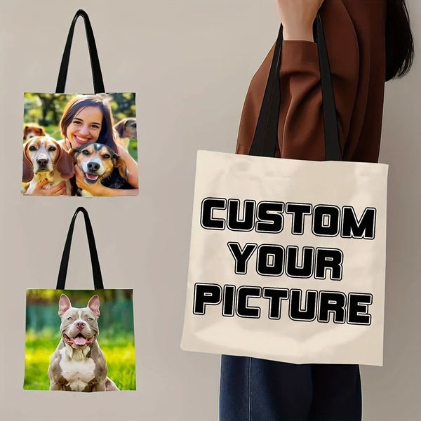 A person holds a beige canvas tote bag with black handles, featuring text that reads Custom Your Picture.