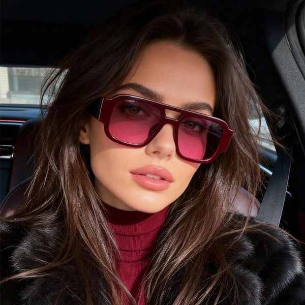 A woman wearing vintage leopard print oversized square sunglasses and a red turtleneck in a car interior.