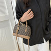A tan and brown patterned fashion shell shoulder crossbody bag carried by a person wearing a black top.