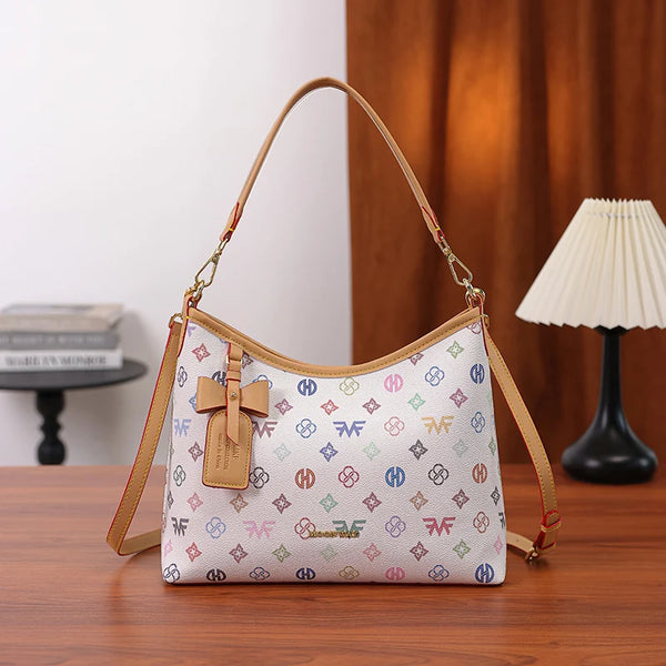 A beige crescent tote bag with a letter print and bow accent resting on a wooden surface.