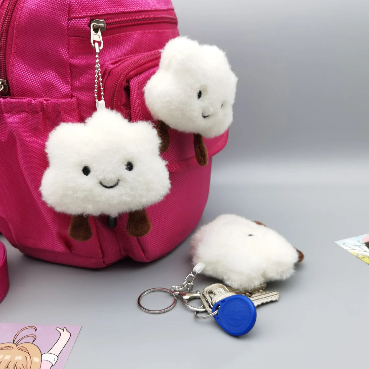 A pink backpack features two white fluffy cloud plush charms attached to a silver keychain.