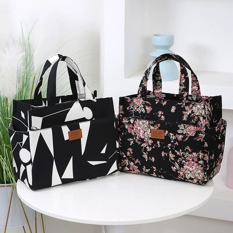 A black cloth tote bag with a pink floral pattern is displayed on a white shelf.