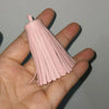 A hand holds a pink leather tassel fringe craft supplies set with long, thin strands.