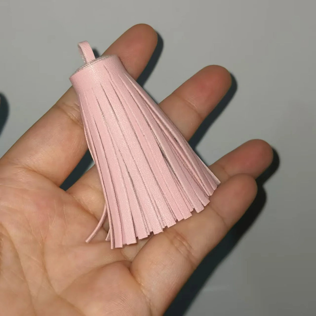 A hand holds a pink leather tassel fringe craft supplies set with long, thin strands.