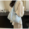 A light striped canvas shoulder bag with a magnetic closure is displayed next to a white garment.