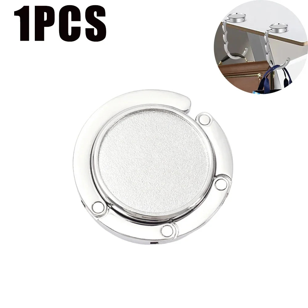 Gancho de bolsa plegable plateado diseñado para organizar artículos en una mesa o bolso.
