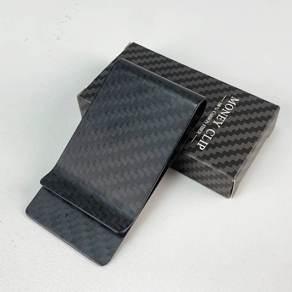 A black carbon fiber money clip is displayed in its box, showing the texture and branding.