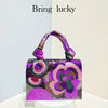 A purple and pink sequin embroidered floral clutch bag with a purple strap displayed on a white pedestal.