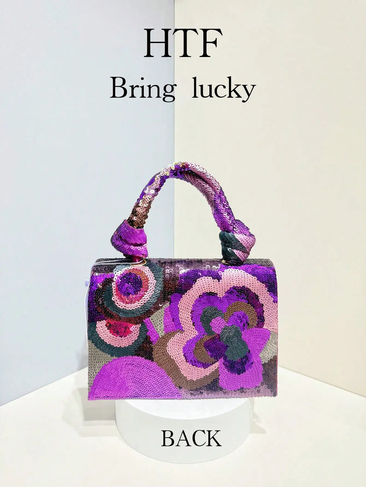 A purple and pink sequin embroidered floral clutch bag with a purple strap displayed on a white pedestal.