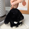 A small black plush rabbit with white accents is held by a hand, displayed on a light surface.