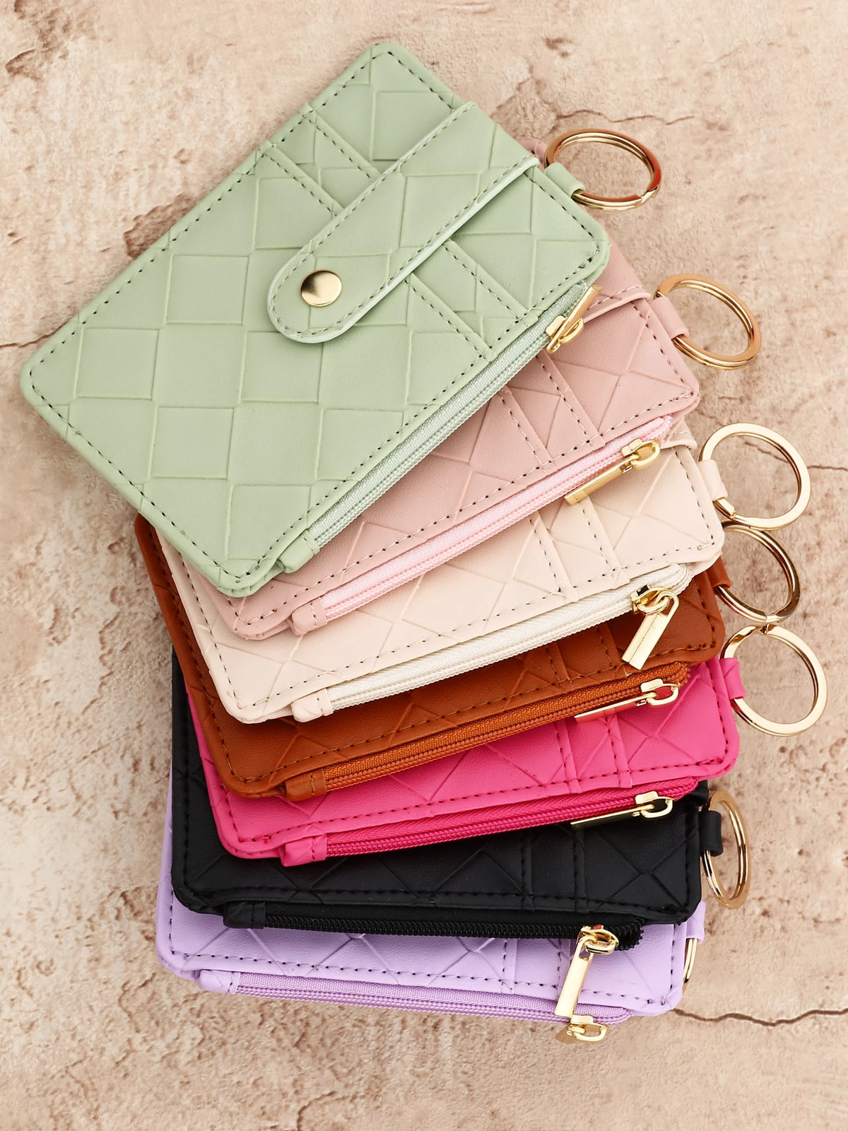A stack of five pastel quilted PU leather card holder wallets in mint green, pink, beige, brown, and purple with gold-toned b