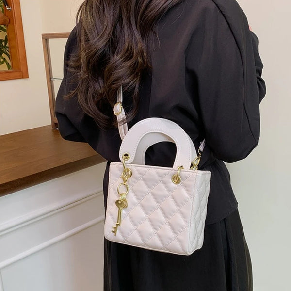 A white quilted crossbody handbag with a gold chain accent is carried by a person wearing a black coat.