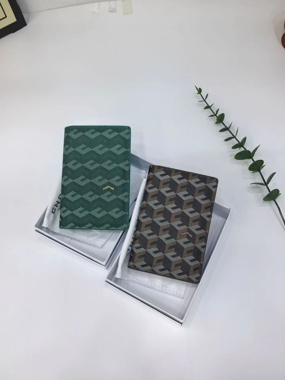 A dark green geometric print passport wallet displayed in a clear presentation box on a white surface.