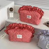 A red and white checkered makeup pouch with a ruffled lace trim is displayed on a white shelf.